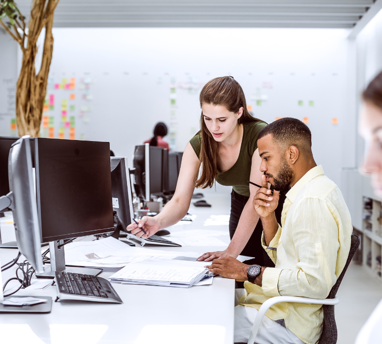 Woman standing at a desk next to a man sitting working at his desk.